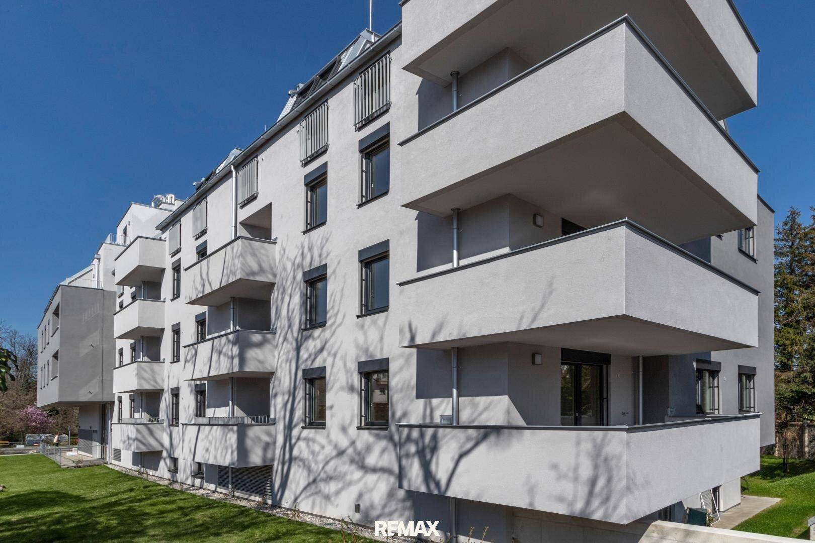Seitenansicht eines modernen Mehrfamilienhauses mit zahlreichen Balkonen und gepflegter Grünfläche.