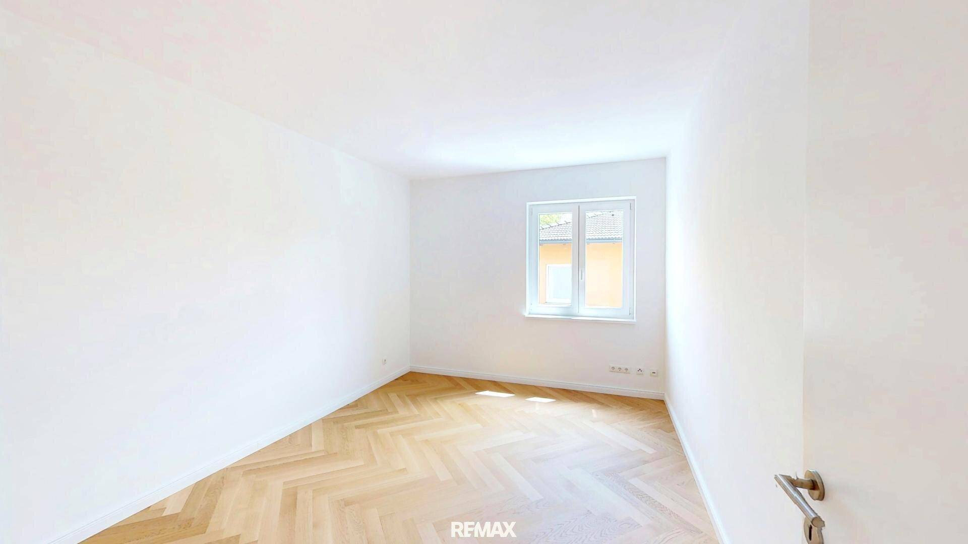 Helles Schlafzimmer mit Fischgrätparkett und Fenster, das viel natürliches Licht hereinlässt.