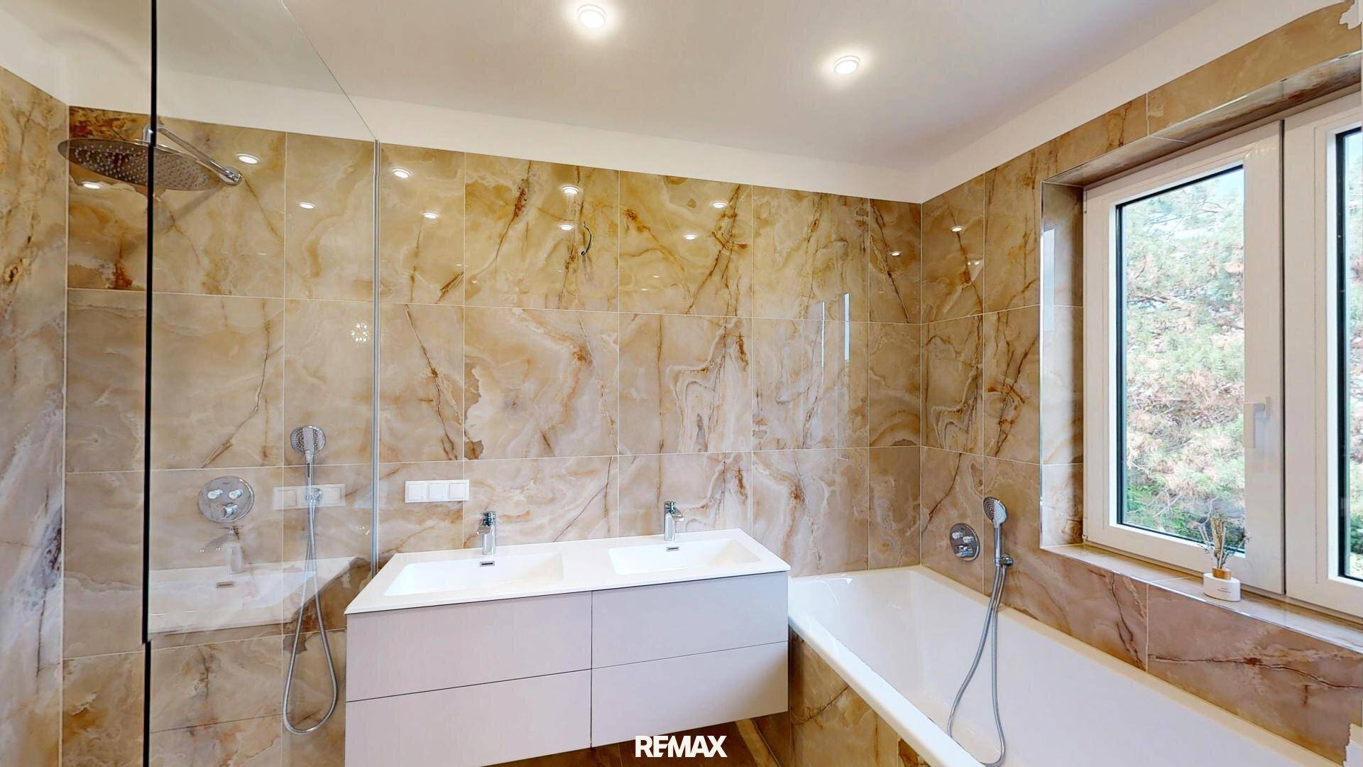 Helles Badezimmer mit Badewanne, Dusche, Doppelwaschbecken und Fenster für Tageslicht.
