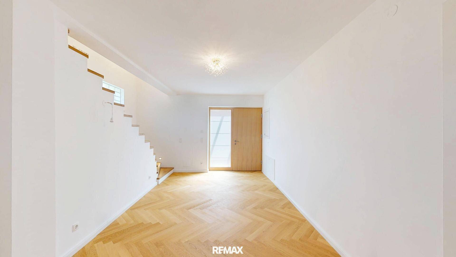 Eingangsbereich mit hellem Fischgrätparkett und moderner Holztür, die viel Licht hereinlässt.