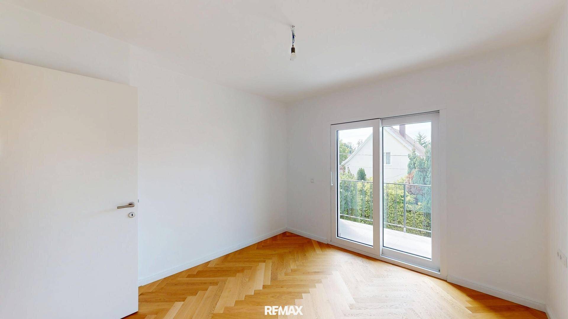 Geräumiges Schlafzimmer mit Fischgrätparkett und Zugang zu einem französischen Balkon.