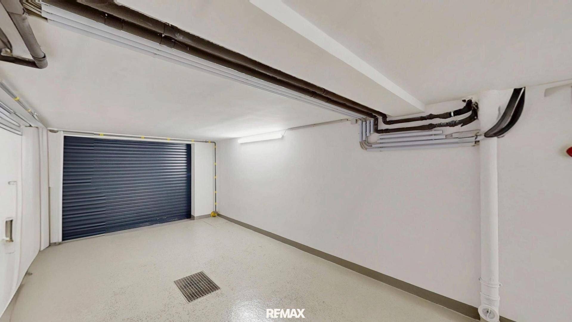 Geräumige Garage mit dunklem Rolltor und hellem, pflegeleichtem Boden, ideal für Fahrzeuge.