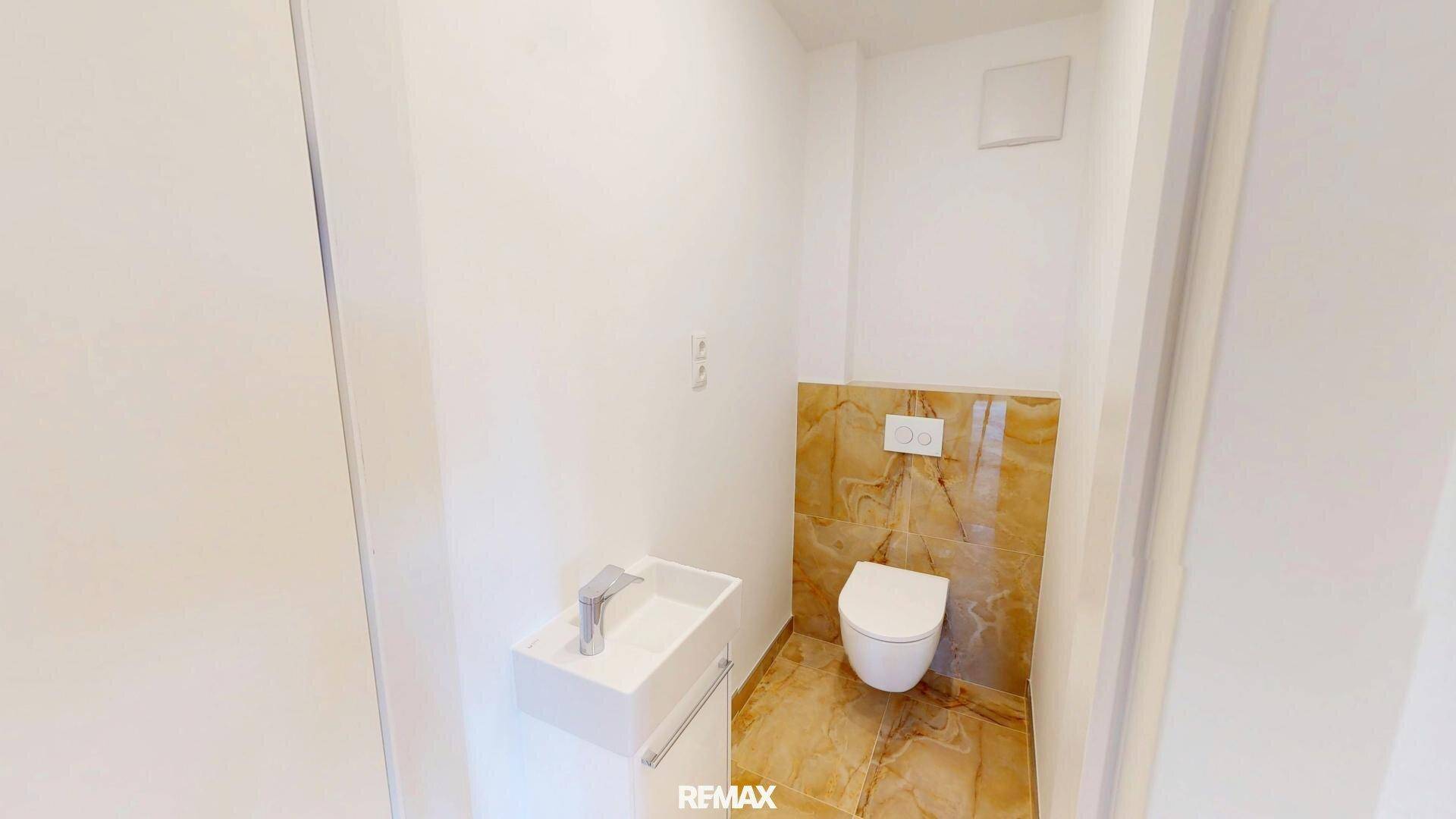 Modernes Gäste-WC mit wandhängendem WC, kleinem Waschbecken und eleganten Marmorfliesen.