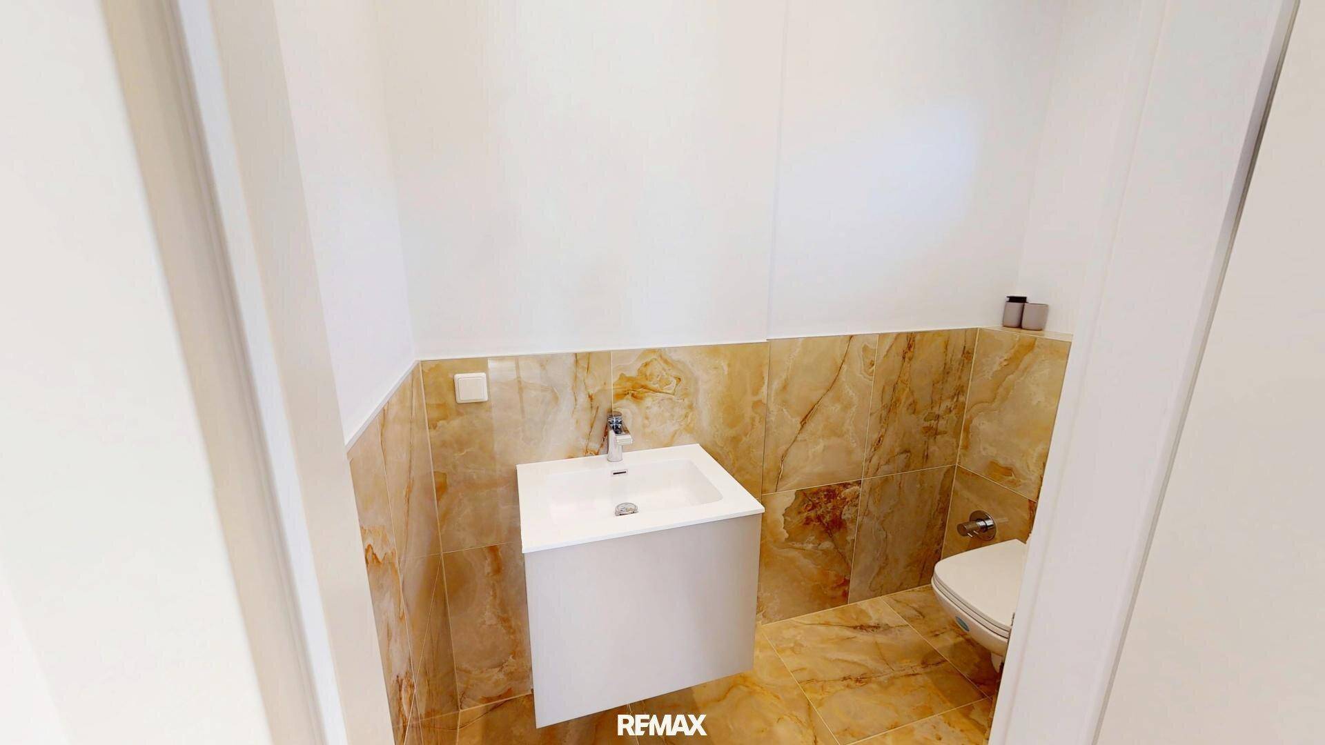 Modernes Gäste-WC mit eleganten Marmorfliesen, wandhängendem WC und kleinem Waschbecken.