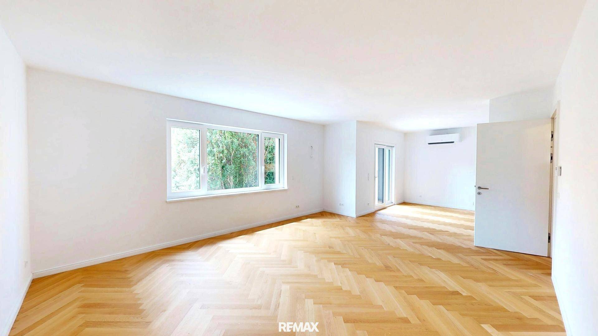 Lichtdurchfluteter Raum mit Fischgrätparkett, Klimaanlage und Zugang zu einem Balkon oder einer Terrasse.
