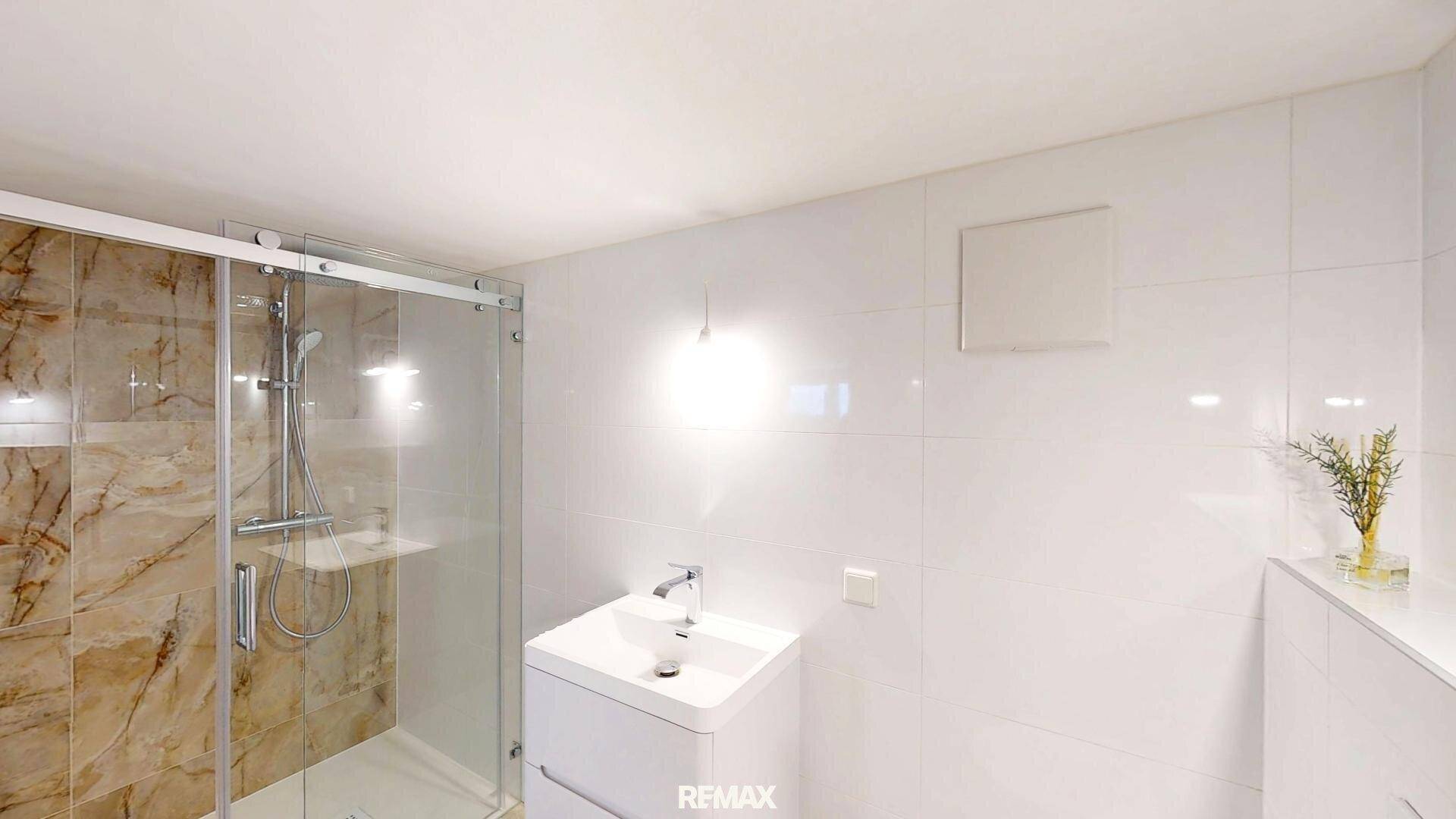 Modernes Badezimmer mit weißen Fliesen, Einzelwaschbecken und einer geräumigen Duschkabine.