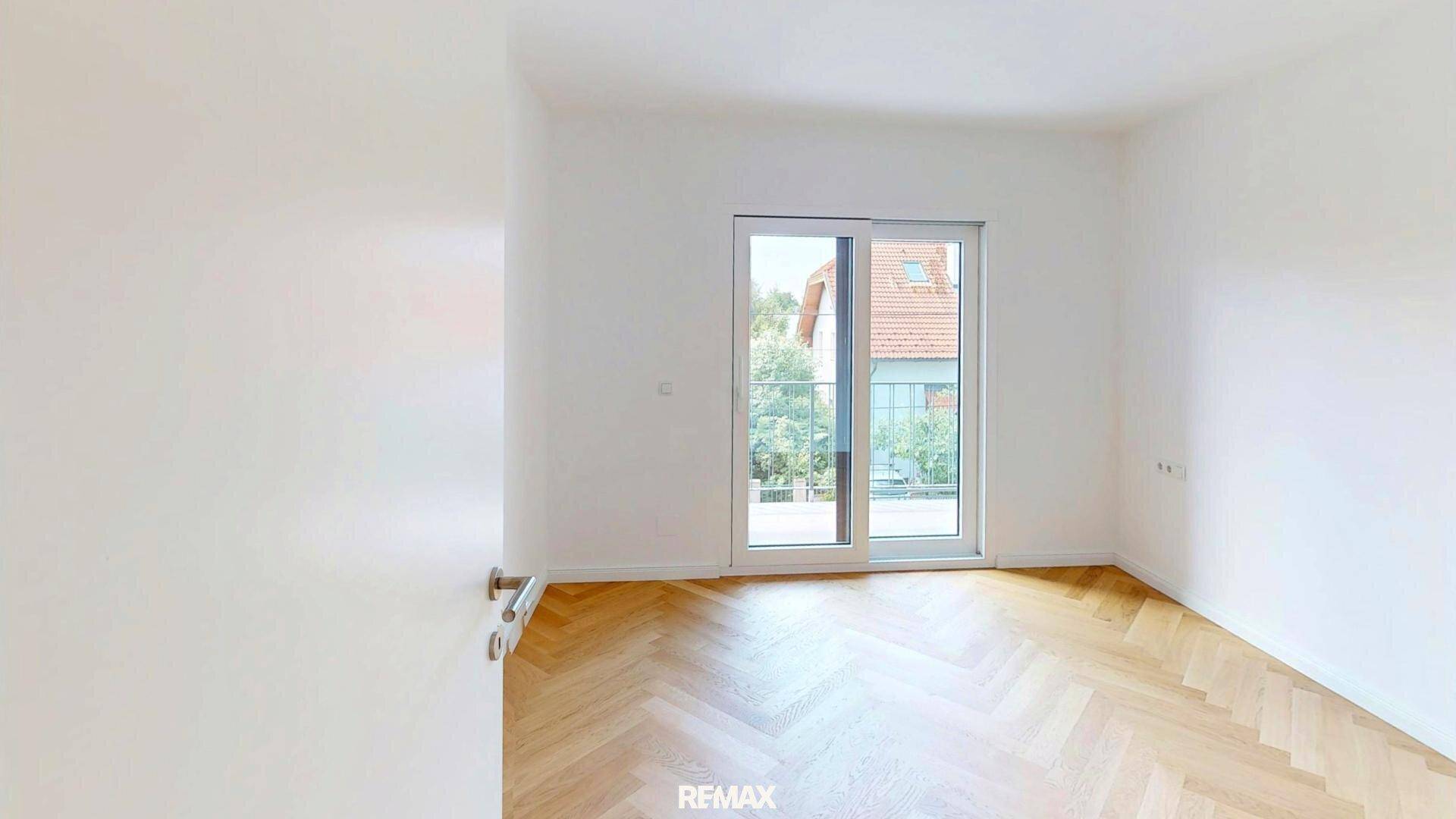 Helles Schlafzimmer mit Fischgrätparkett und Zugang zu einem französischen Balkon mit Blick ins Grüne.