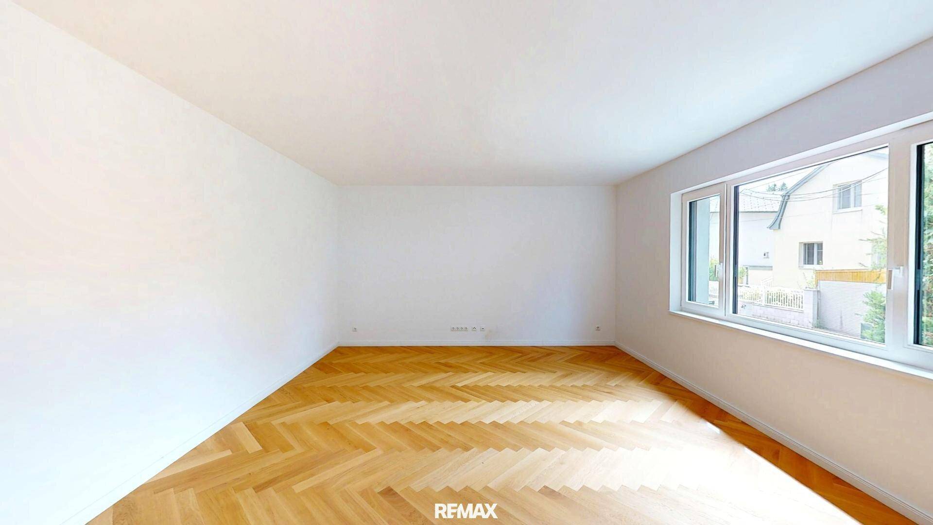 Heller, leerer Raum mit Fischgrätparkett und großen Fenstern, die viel Tageslicht hereinlassen.