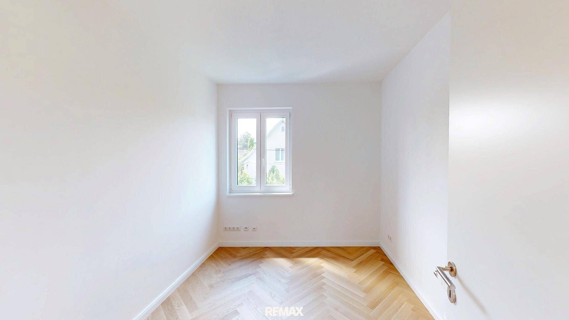 Helles Schlafzimmer mit Fischgrätparkett und Fenster, das viel Tageslicht hereinlässt.