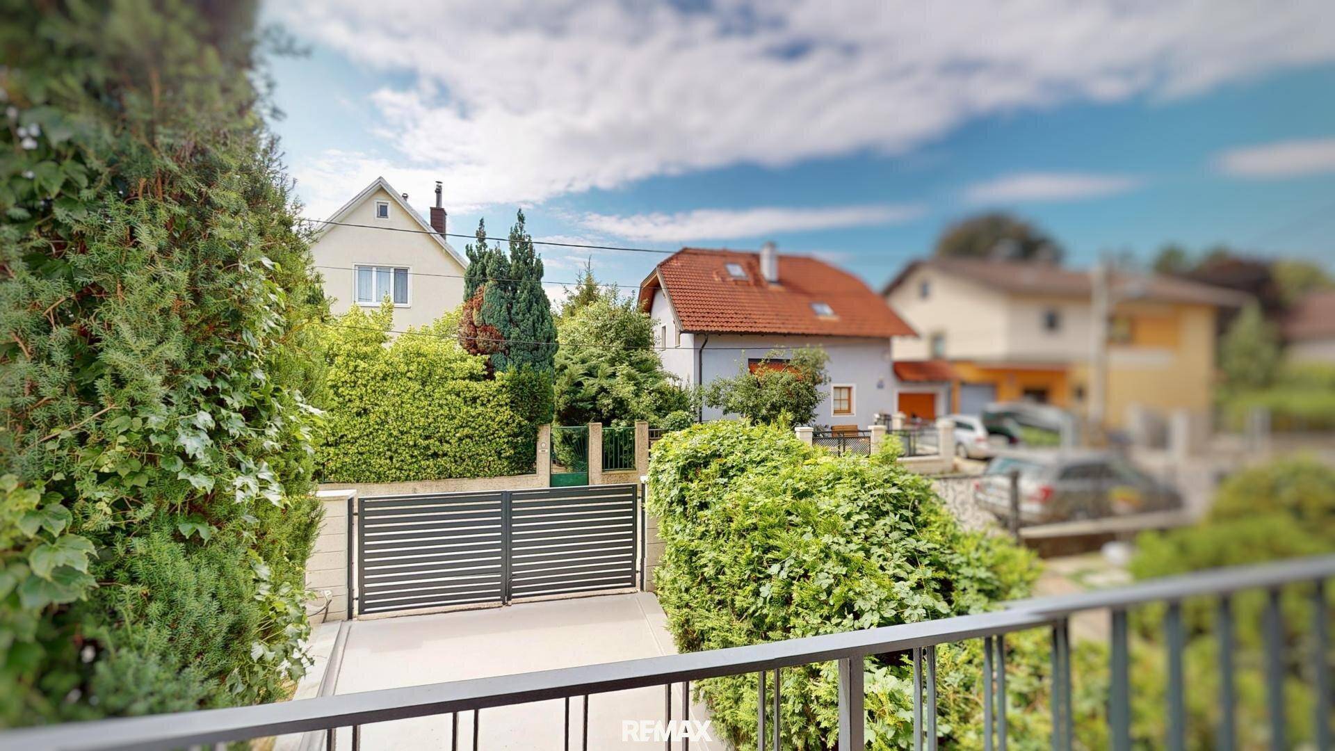 Blick von einem Balkon auf die Einfahrt mit modernem Tor und gepflegten Hecken.