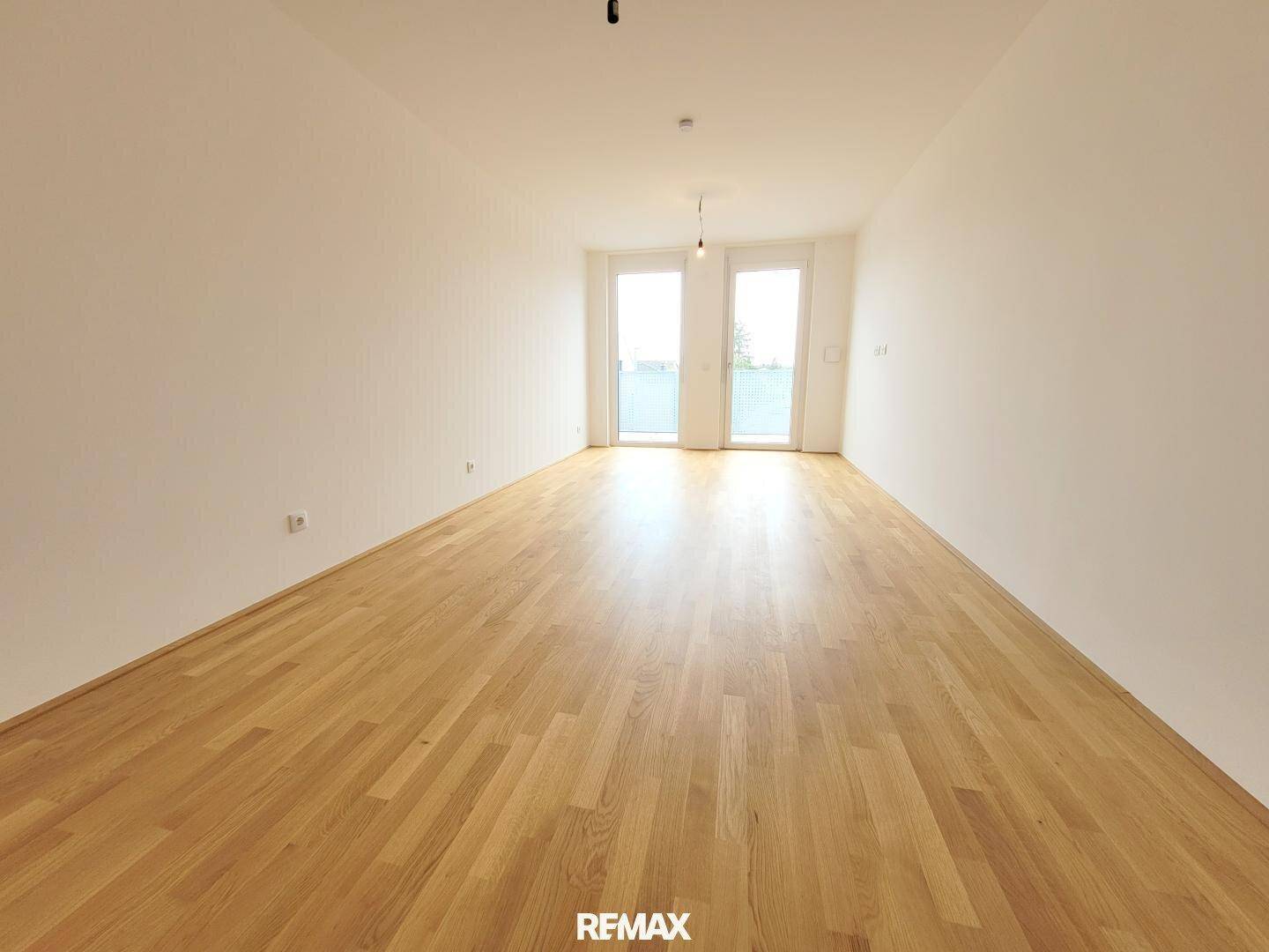 Heller, leerer Raum mit hellem Parkettboden und Zugang zu einem Balkon.