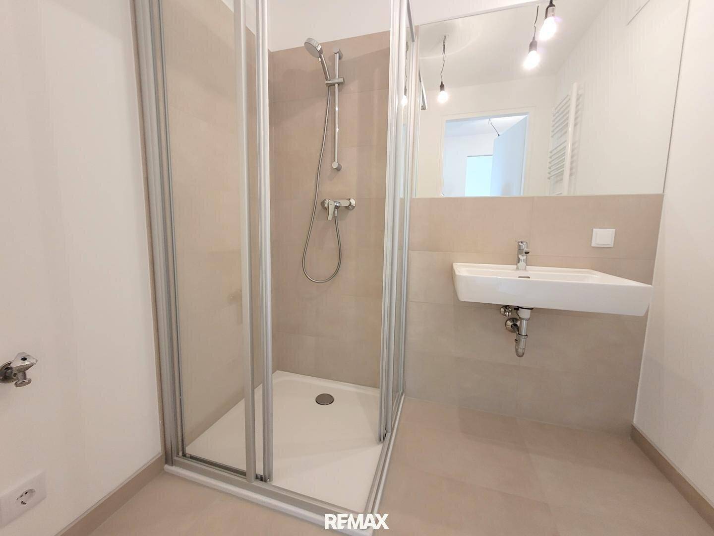 Modernes Badezimmer mit Duschkabine, Einzelwaschbecken und hellen Fliesen.