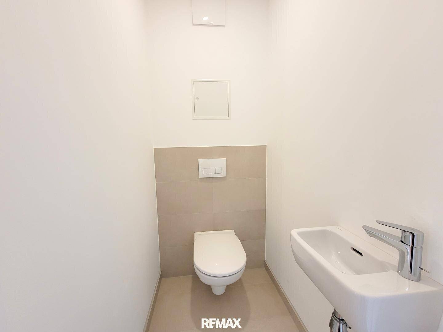 Separates Gäste-WC mit wandhängender Toilette und kleinem Handwaschbecken.