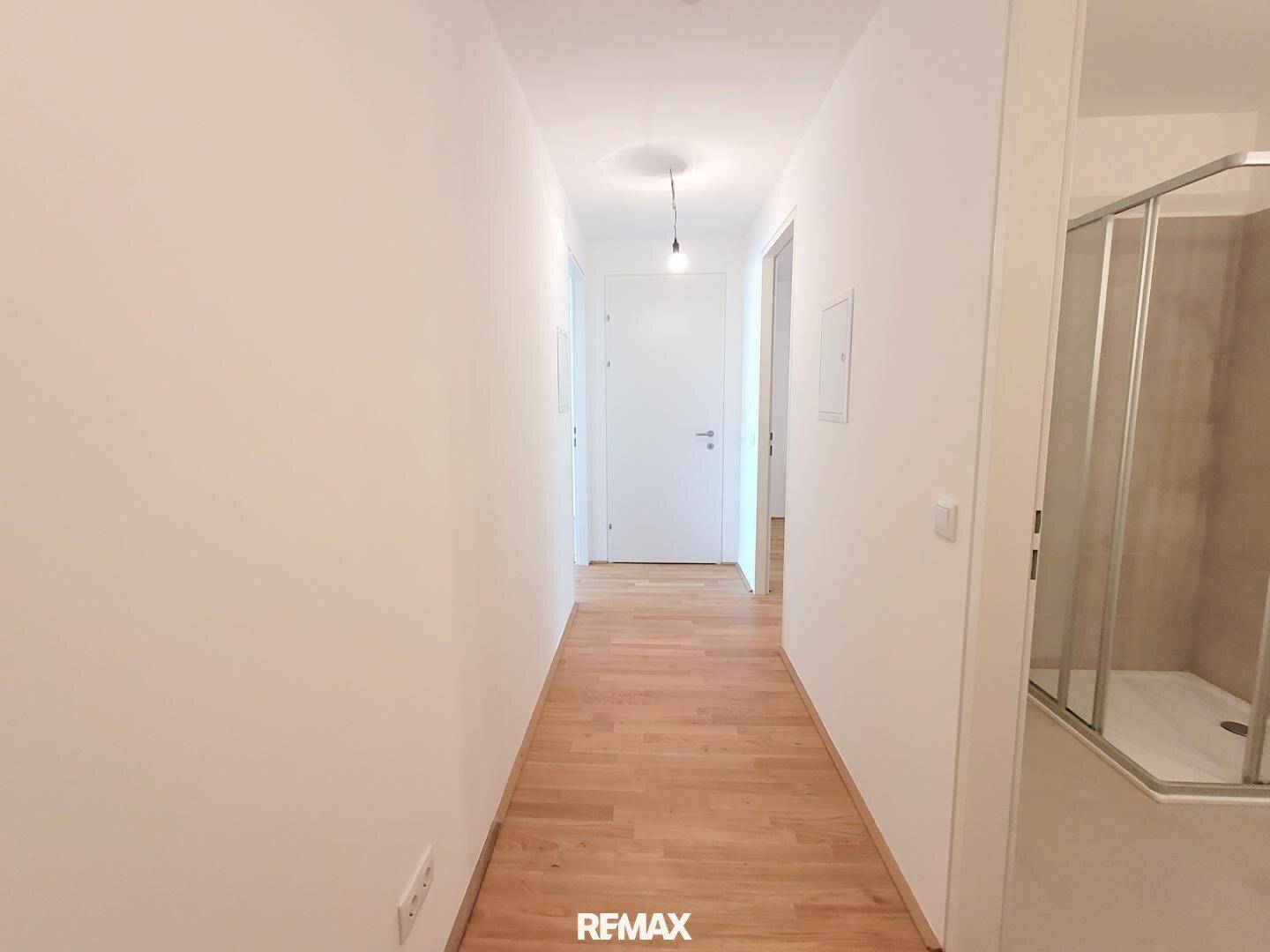 Heller Flur mit Parkettboden, weißen Wänden und Zugang zu verschiedenen Räumen, inklusive Bad.