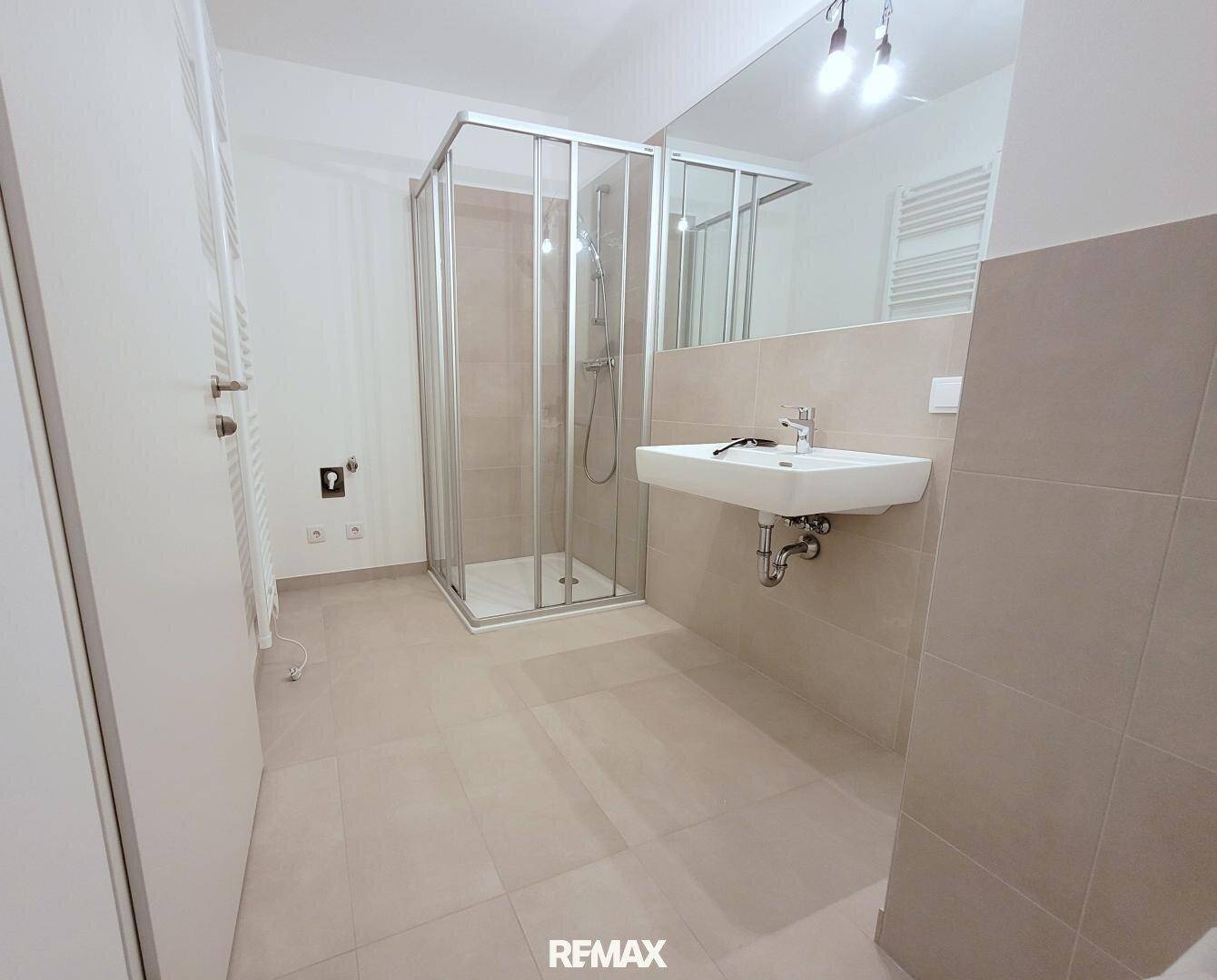 Modernes Badezimmer mit Duschkabine, Waschbecken, großem Spiegel und beheiztem Handtuchhalter.