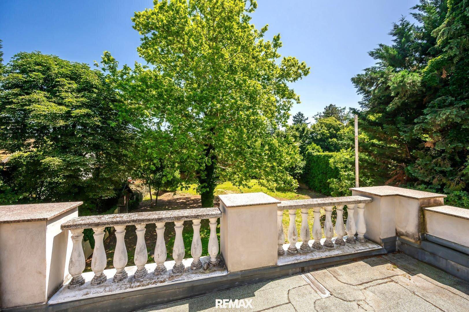Geräumige Terrasse mit klassischer Balustrade und weitem Blick ins Grüne unter blauem Himmel.