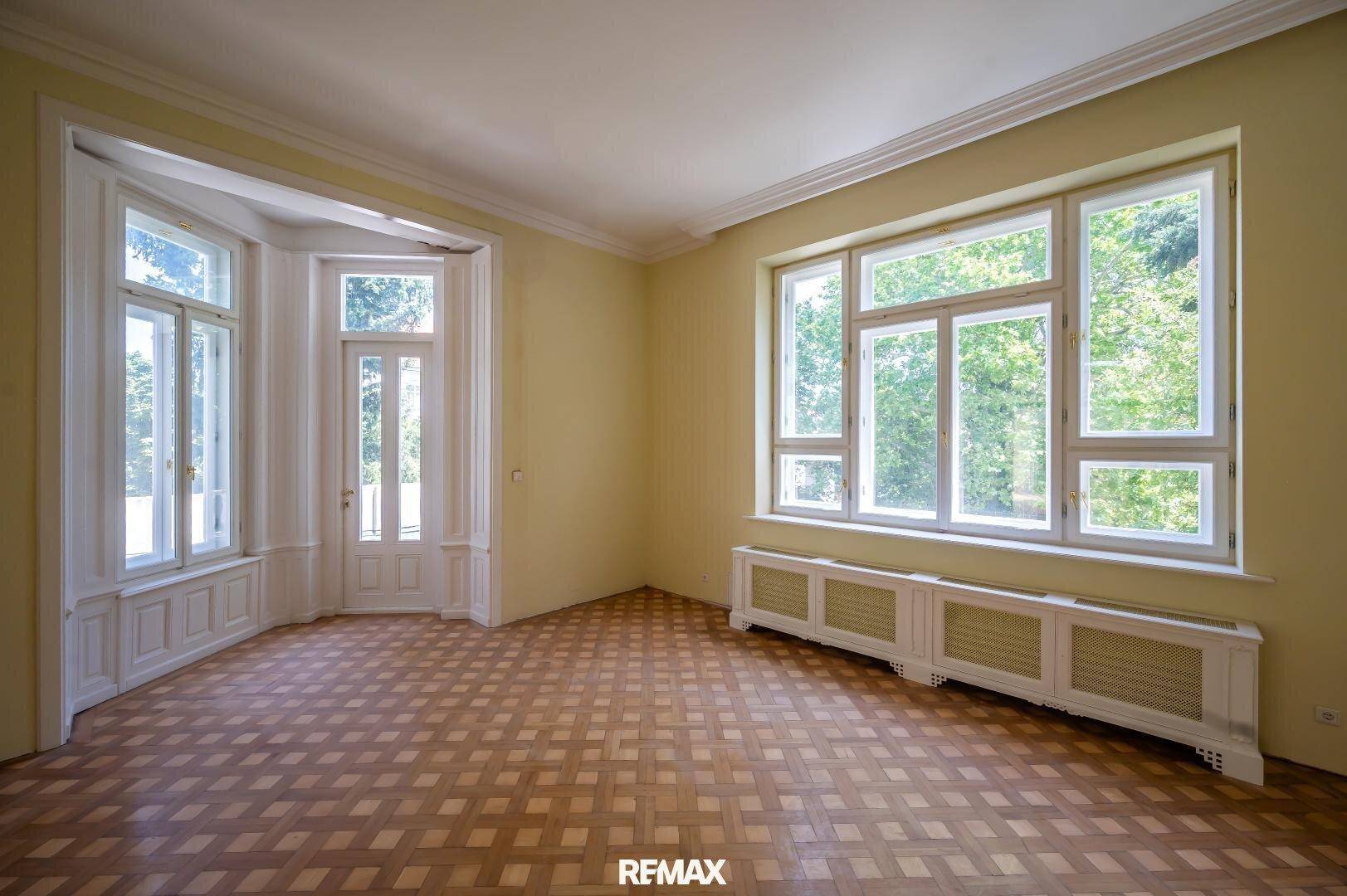 Helles Wohnzimmer mit Parkettboden, Erkerfenster und Blick ins Grüne.