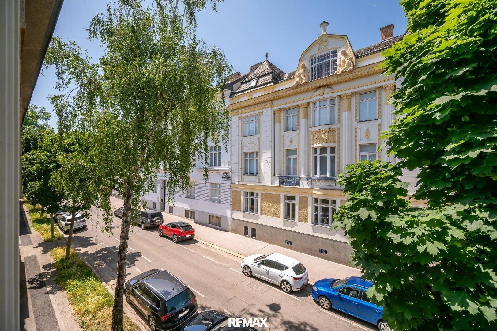 Historisches Gebäude an einer von Bäumen gesäumten Straße mit parkenden Autos.