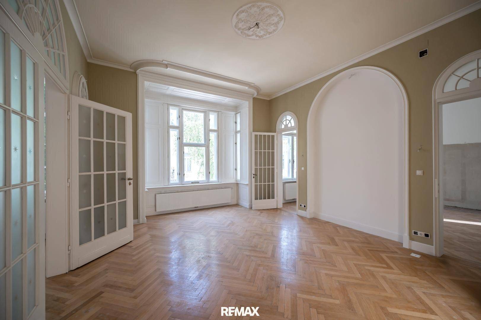 Geräumiges Wohnzimmer mit Fischgrätparkett, Erkerfenster und Stuckdecke.