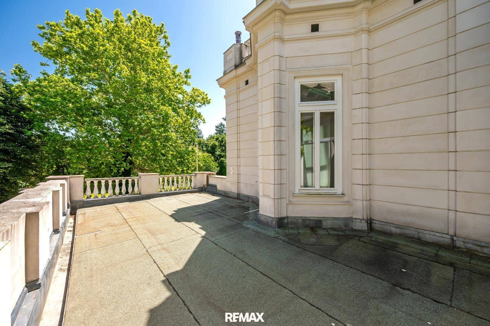 Sonniger Terrassenbereich mit Balustrade und umgebenden Bäumen.