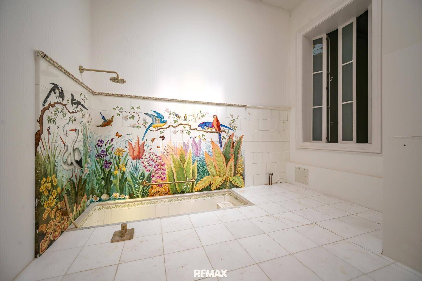 Geräumiges Badezimmer mit gefliestem Boden, eingelassener Wanne und farbenfroher Wandmalerei.