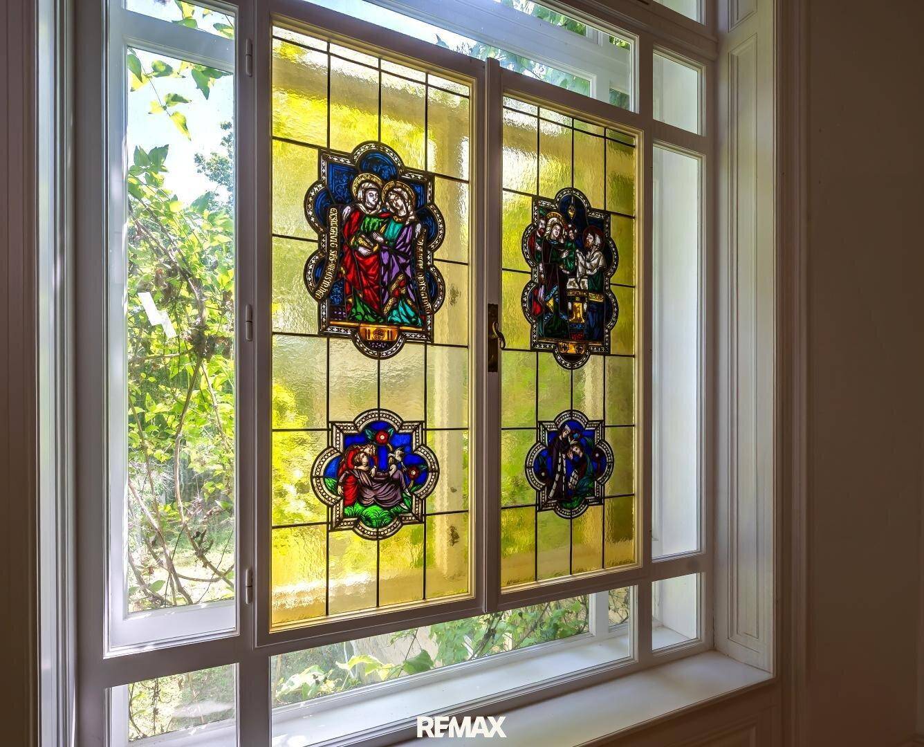Detailansicht eines farbenfrohen Buntglasfensters mit religiösen Motiven und grüner Aussicht.