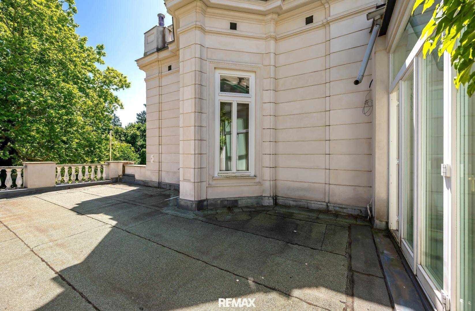 Große Dachterrasse mit Balustrade und Blick auf grüne Bäume.