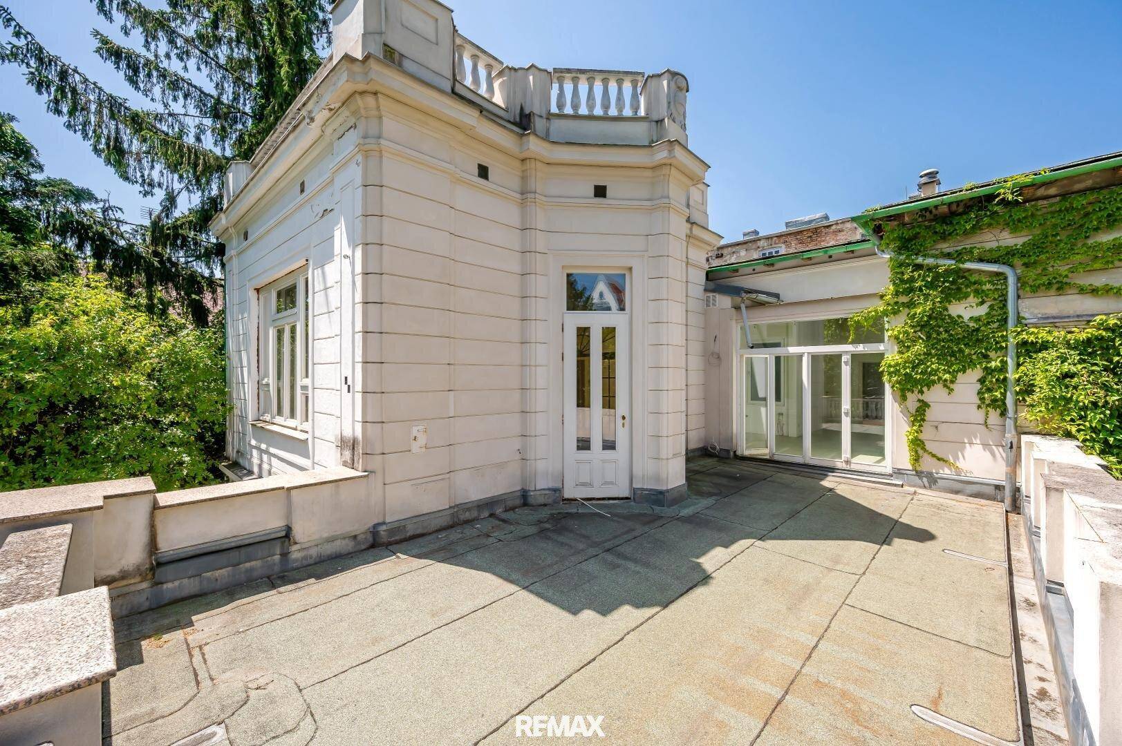 Weitläufige Terrasse an einem historischen Gebäude mit üppiger Vegetation.