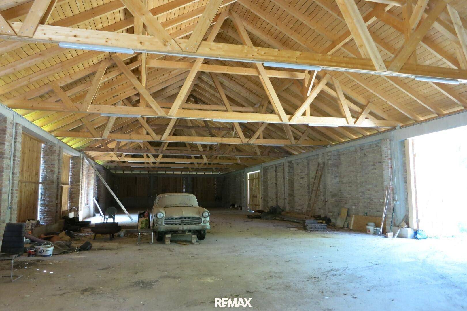Weitläufige Halle mit sichtbarer Holz-Dachkonstruktion und Ziegelwänden, ein klassisches Auto steht im Raum.