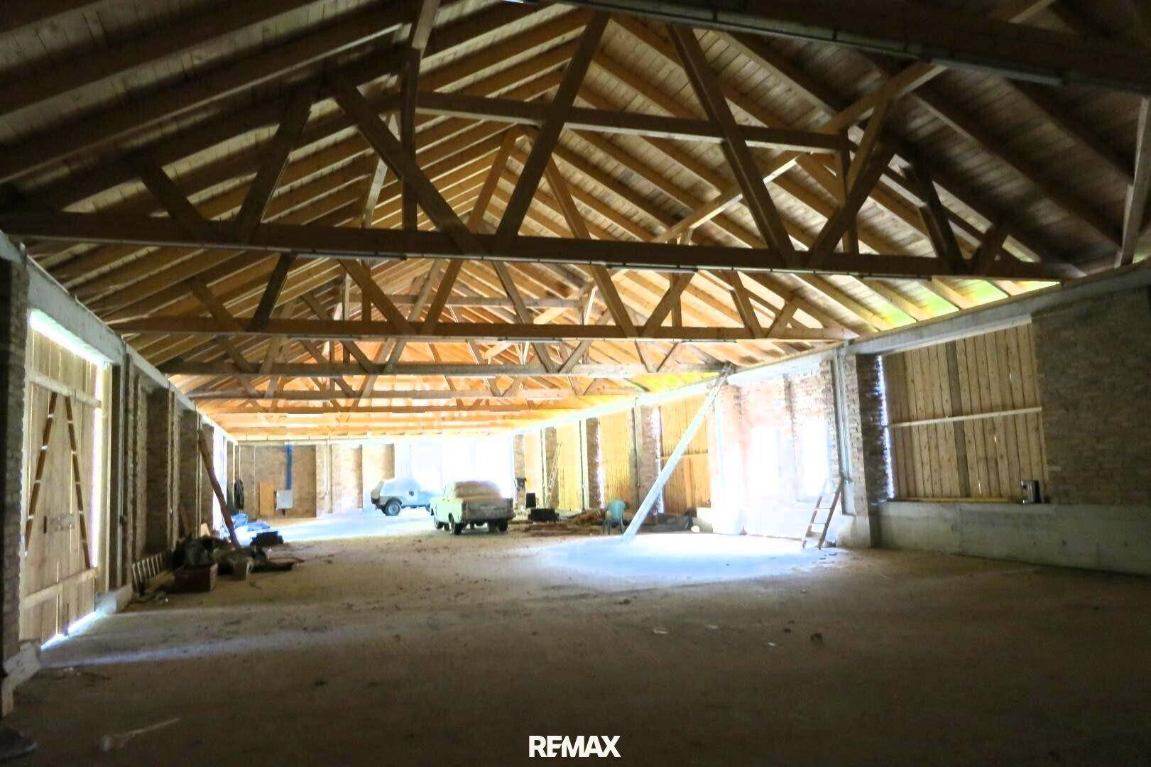 Geräumige Halle mit hoher Holz-Dachkonstruktion und Ziegelwänden, viel Tageslicht fällt herein.