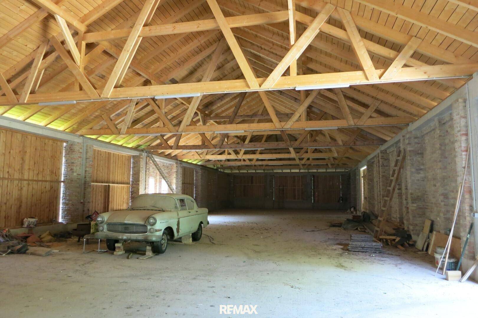 Große, leere Halle mit beeindruckender Holz-Dachkonstruktion und Ziegelwänden, ein altes Auto steht im Vordergrund.