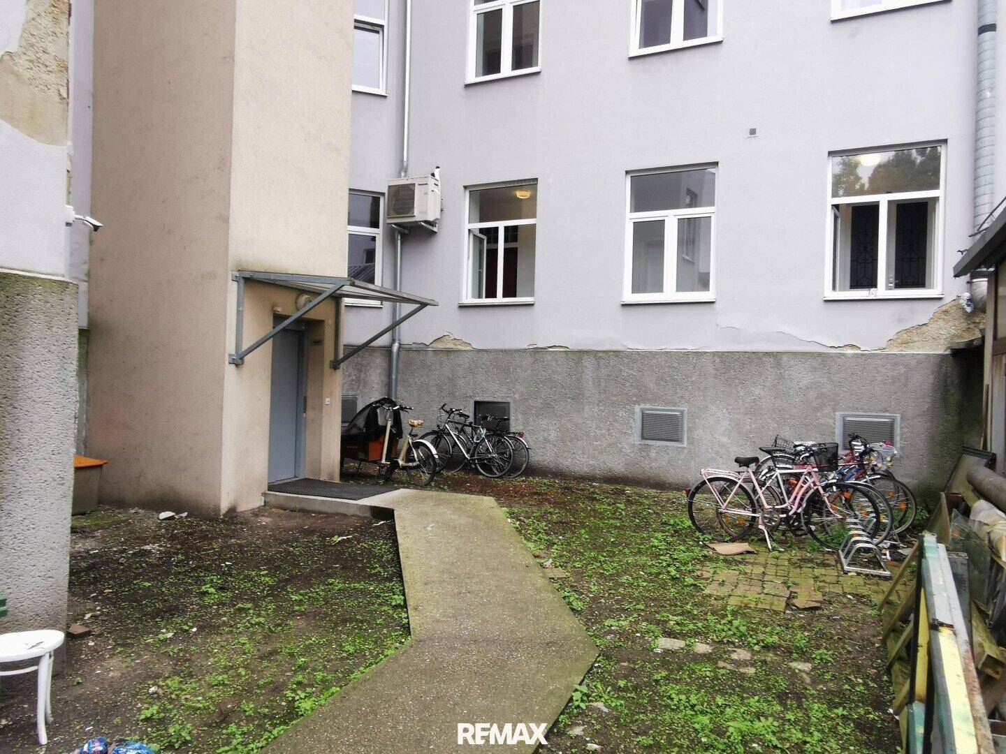 Hinterhof mit Fahrrädern, Grünfläche und der Rückseite des Gebäudes.