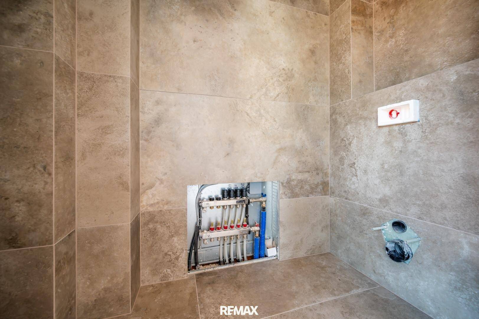Badezimmer im Rohbau mit vorbereiteten Anschlüssen und Fliesenboden, bereit für die Installation.