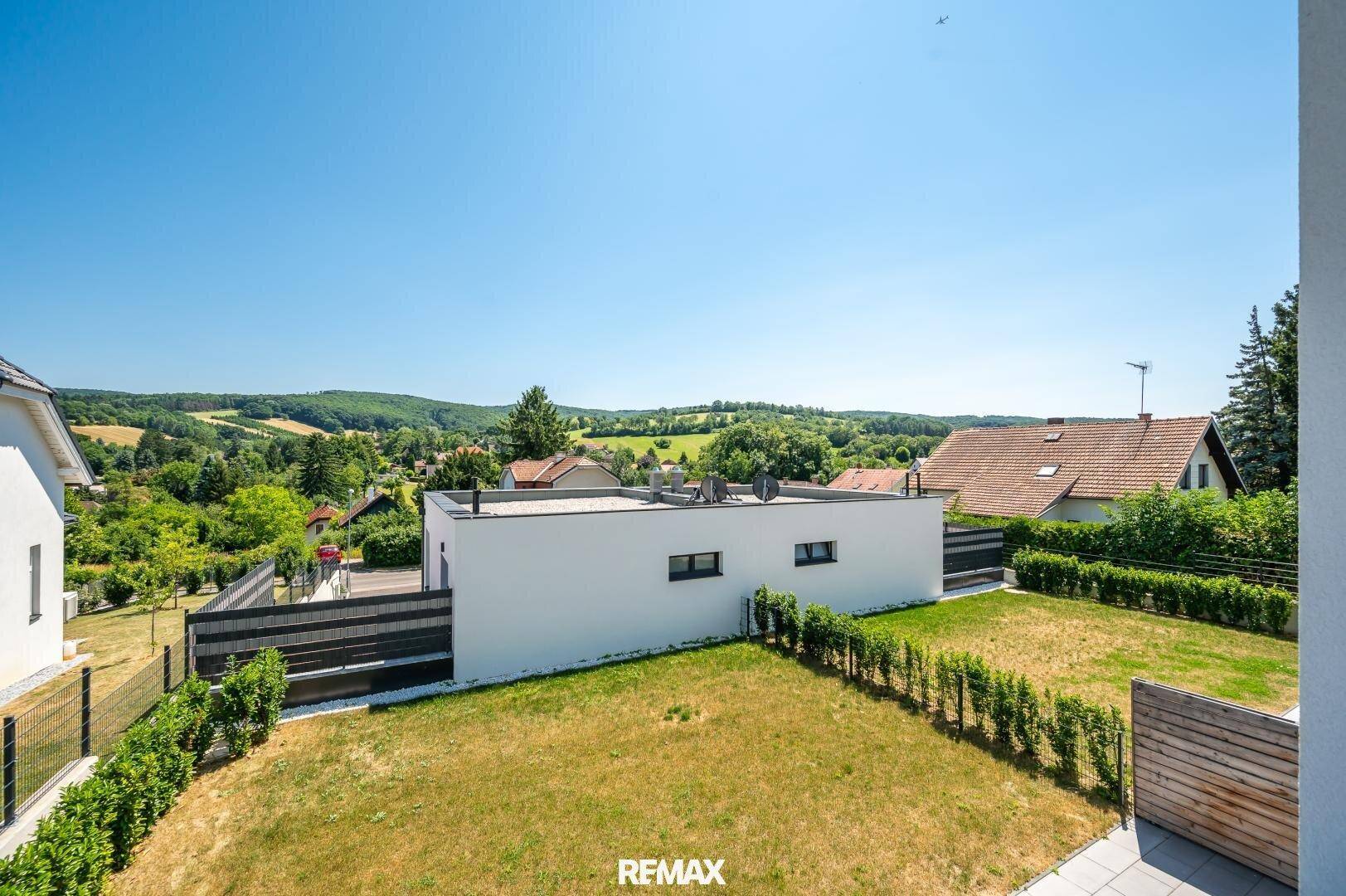 Weitläufiger Blick über die ländliche Umgebung mit dem modernen Neubau und angrenzendem Garten.