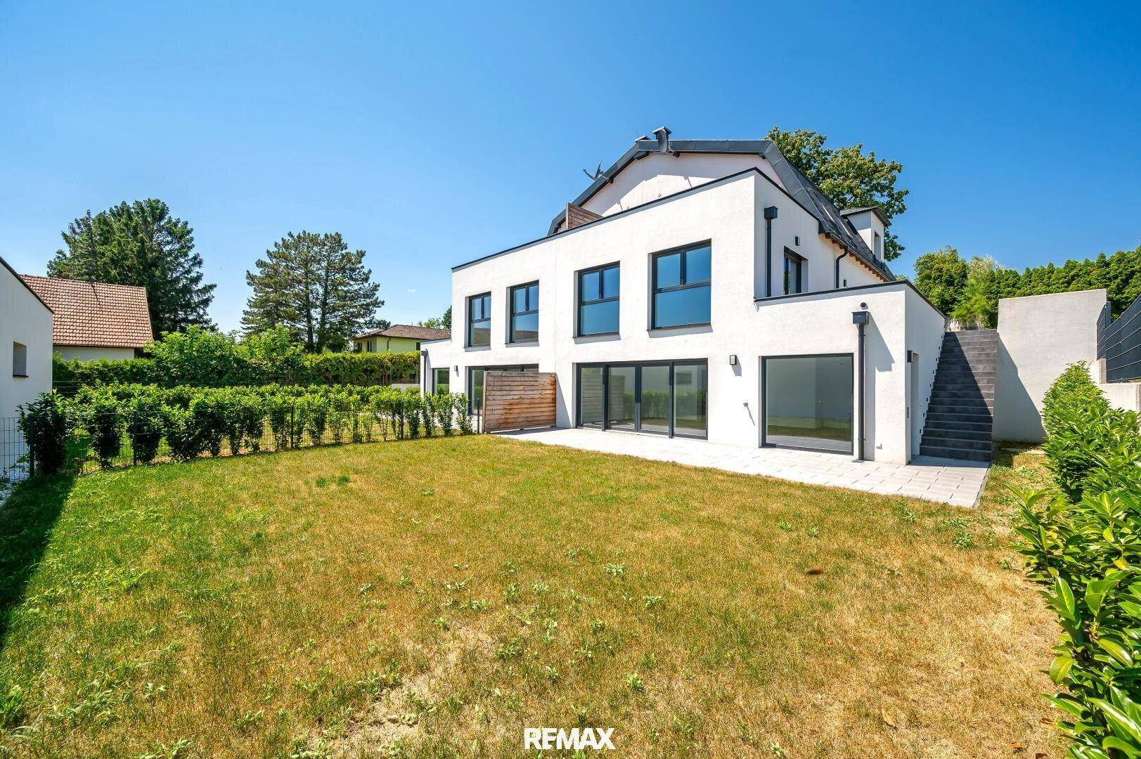 Weitläufiger Gartenbereich mit Rasenfläche und moderner Hausfassade an einem sonnigen Tag.