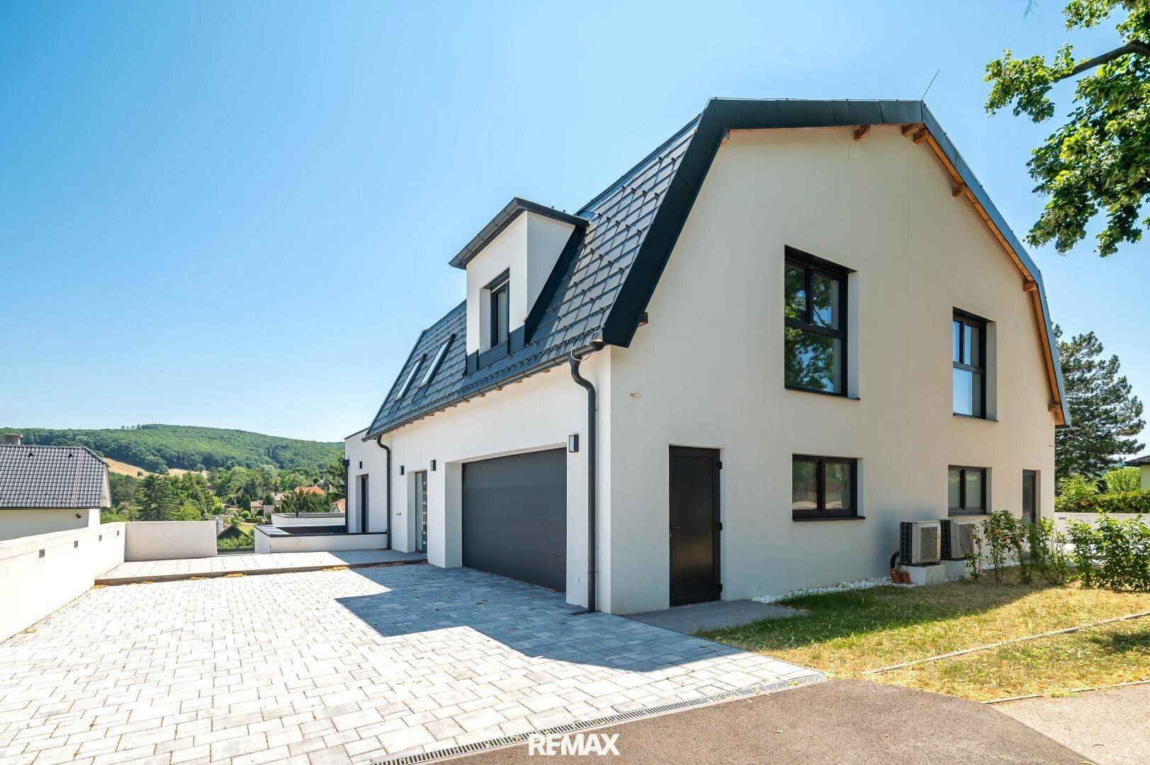 Moderne Hausfassade mit integrierter Doppelgarage und gepflasterter Einfahrt in ländlicher Umgebung.