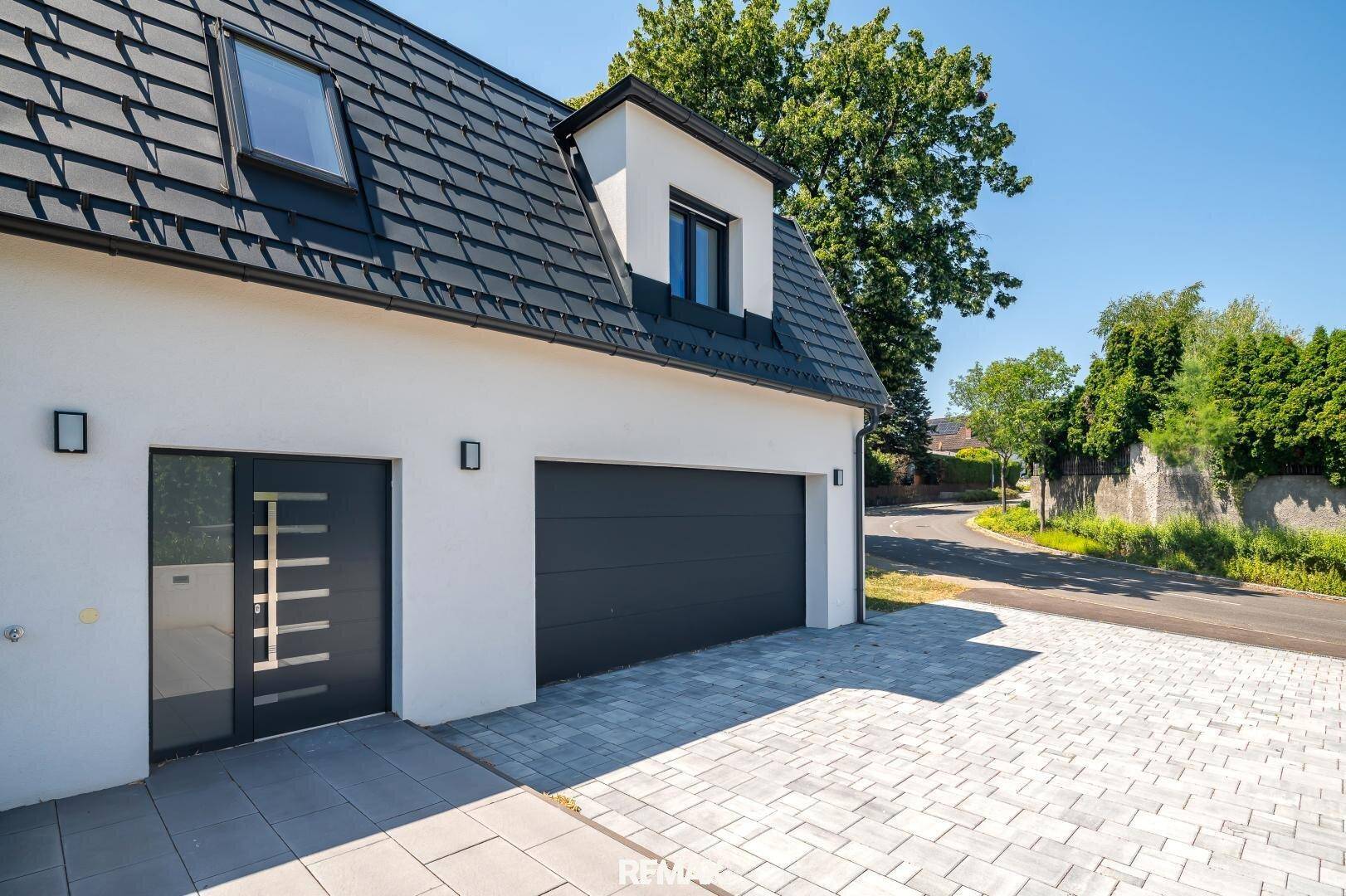 Eingangsbereich mit moderner Haustür und Doppelgarage, umgeben von gepflasterter Einfahrt.