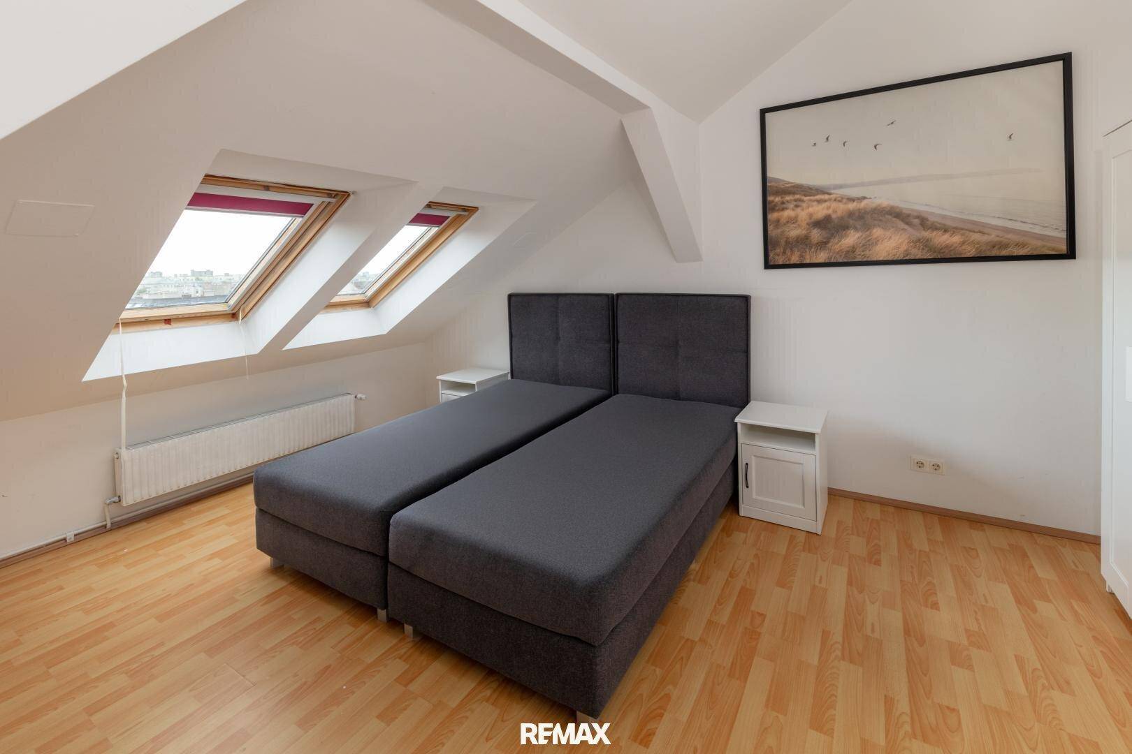 Helles Schlafzimmer mit Dachschrägen, zwei Dachfenstern und einem Doppelbett.