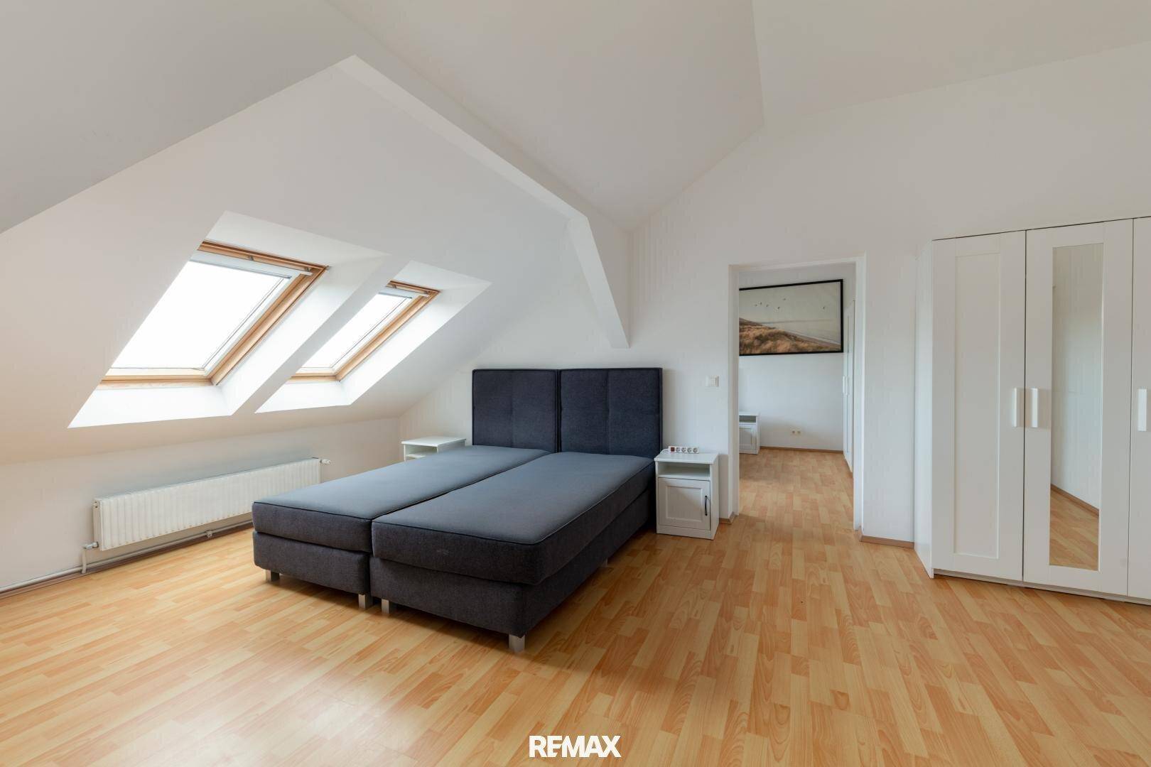 Schlafzimmer im Dachgeschoss mit zwei Dachfenstern, Doppelbett und Holzfußboden.