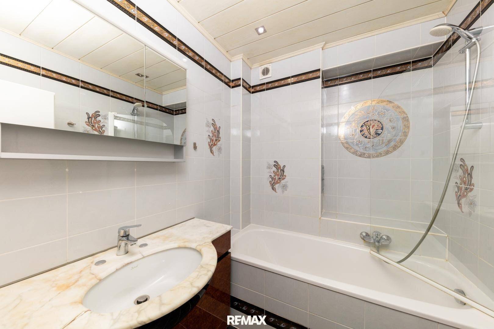 Badezimmer mit Badewanne, Einzelwaschbecken und gefliesten Wänden in hellem Design.
