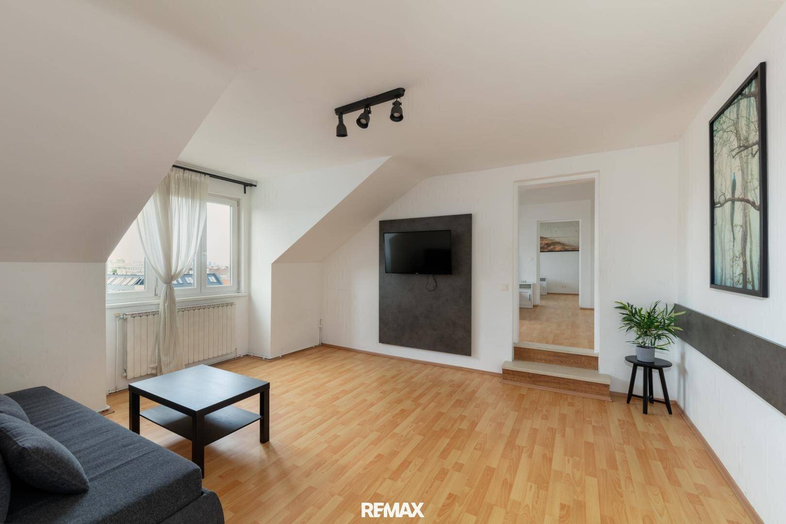 Gemütliches Wohnzimmer im Dachgeschoss mit Schrägen, Holzfußboden und einem Sofa.