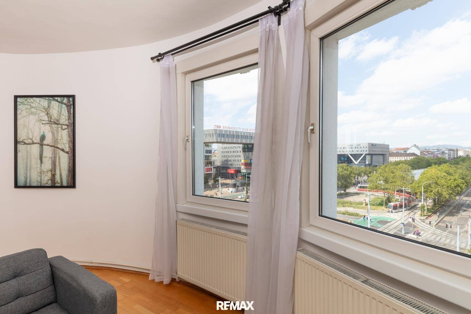 Große Fenster im Wohnzimmer bieten einen weiten Blick auf die belebte Stadtstraße und Grünflächen.