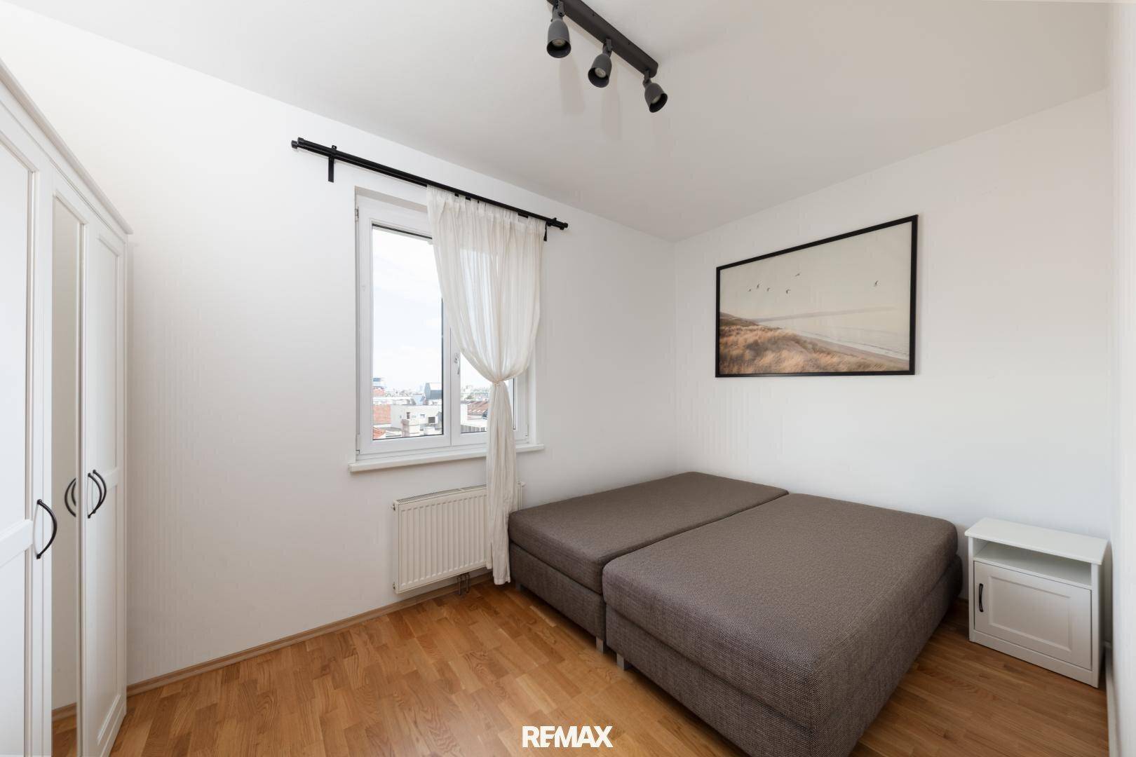 Helles Schlafzimmer mit Holzboden, Kleiderschrank und Fenster mit Stadtblick.
