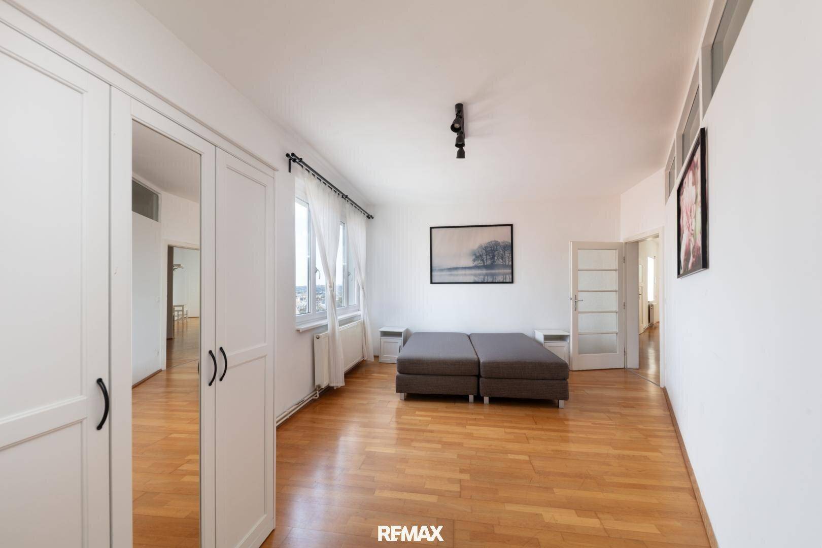 Schlafzimmer mit Spiegelschrank, Holzboden und Zugang zu weiteren Räumen.