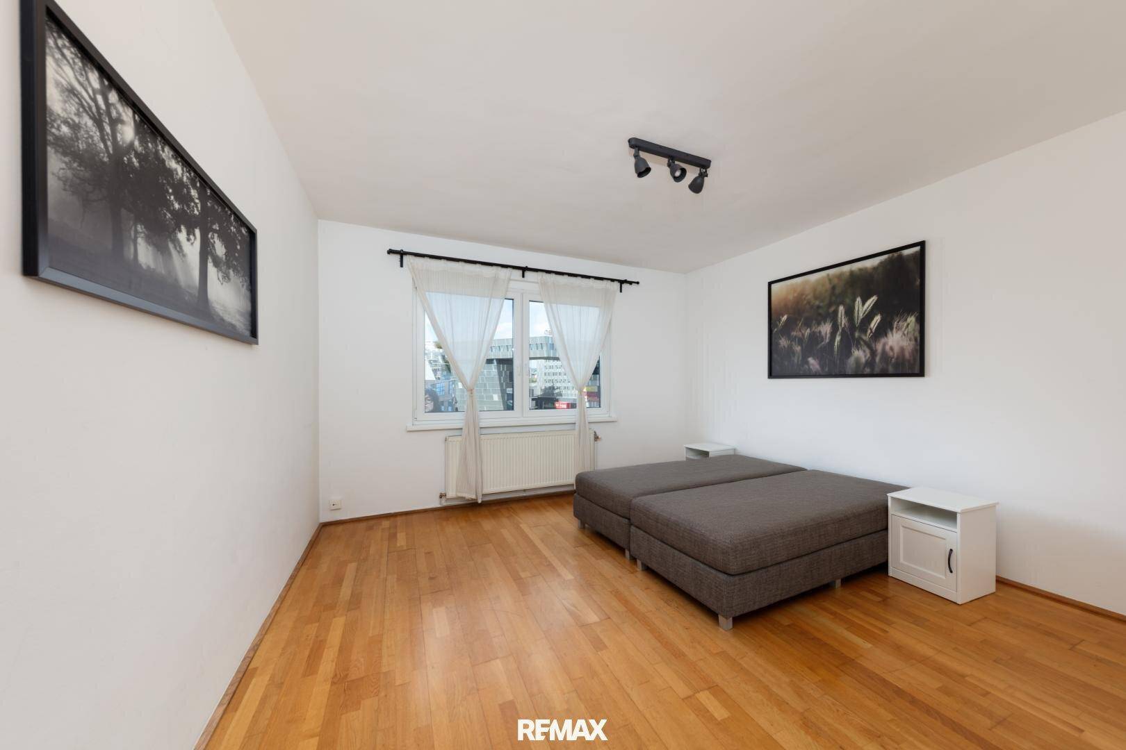 Geräumiges Schlafzimmer mit Holzboden und viel Tageslicht durch das Fenster mit Stadtblick.