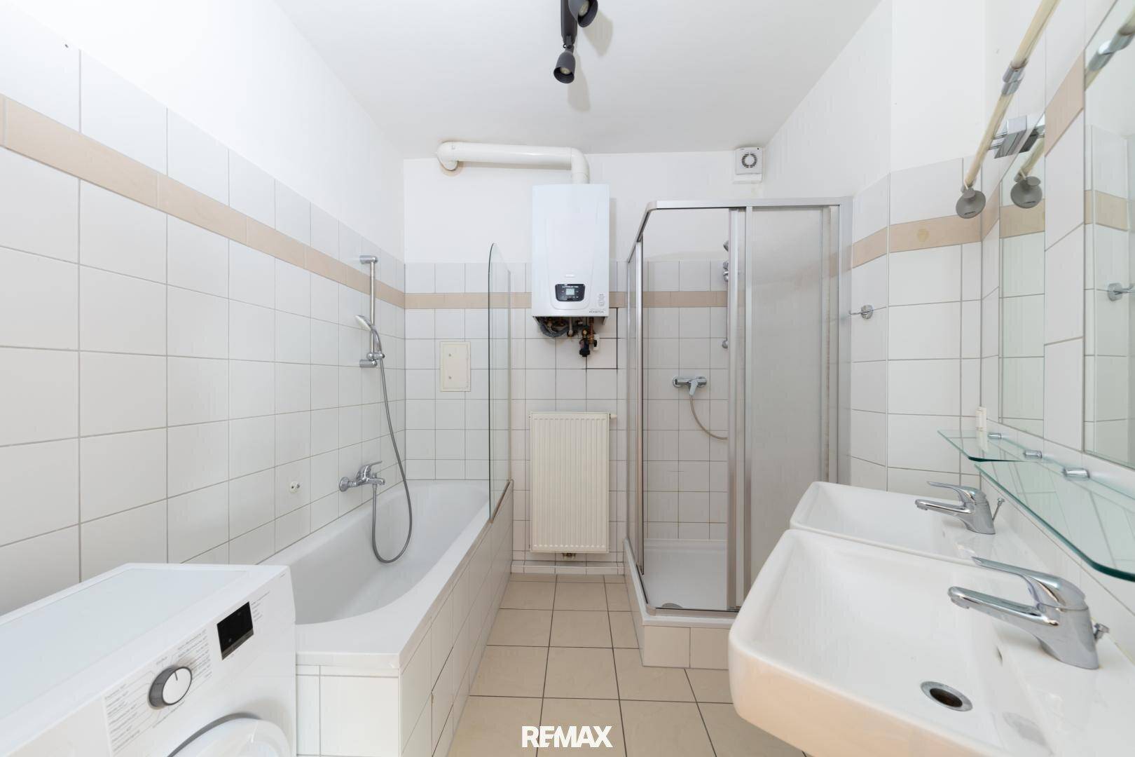 Funktionales Badezimmer mit Badewanne, Duschkabine, Doppelwaschbecken und Waschmaschine.