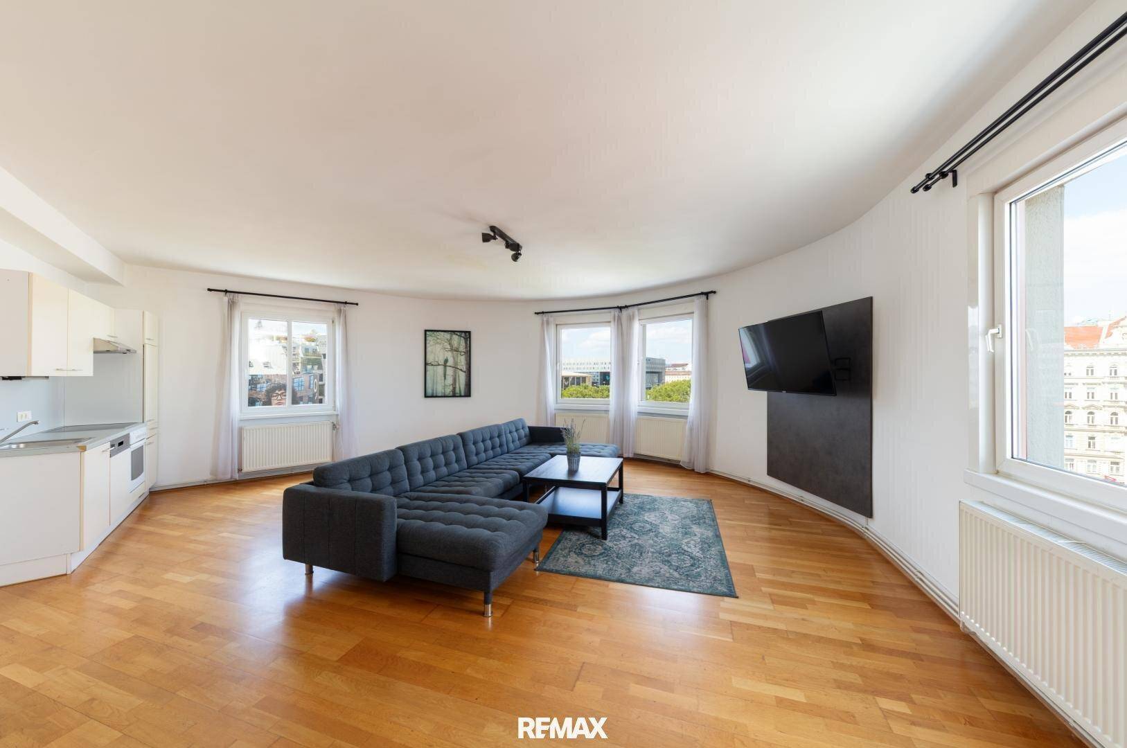 Offener Wohnbereich mit integrierter Küchenzeile, Holzboden und Panoramablick auf die Stadt.