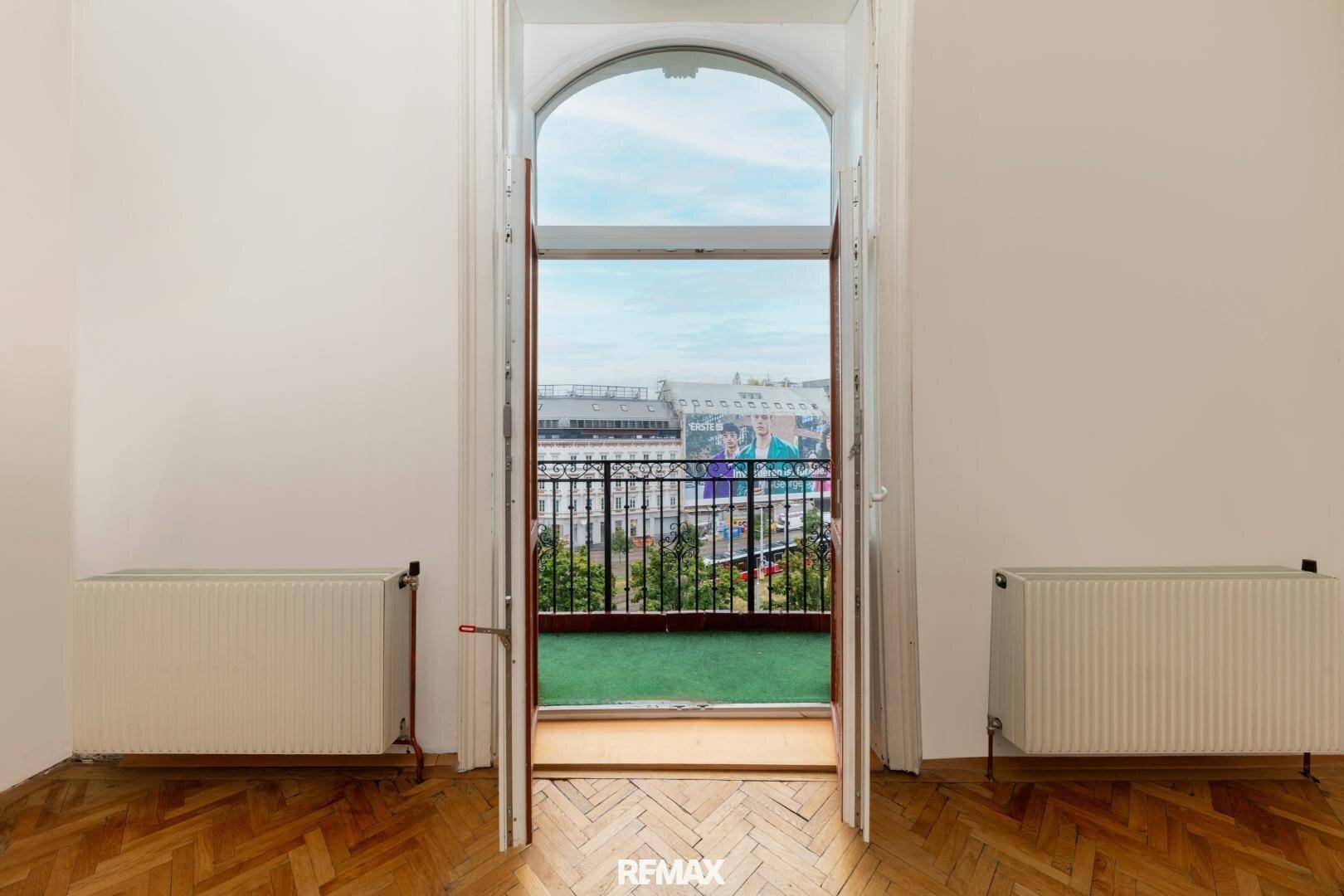 Blick aus einem hohen Bogenfenster auf einen kleinen Balkon mit schmiedeeisernem Geländer.