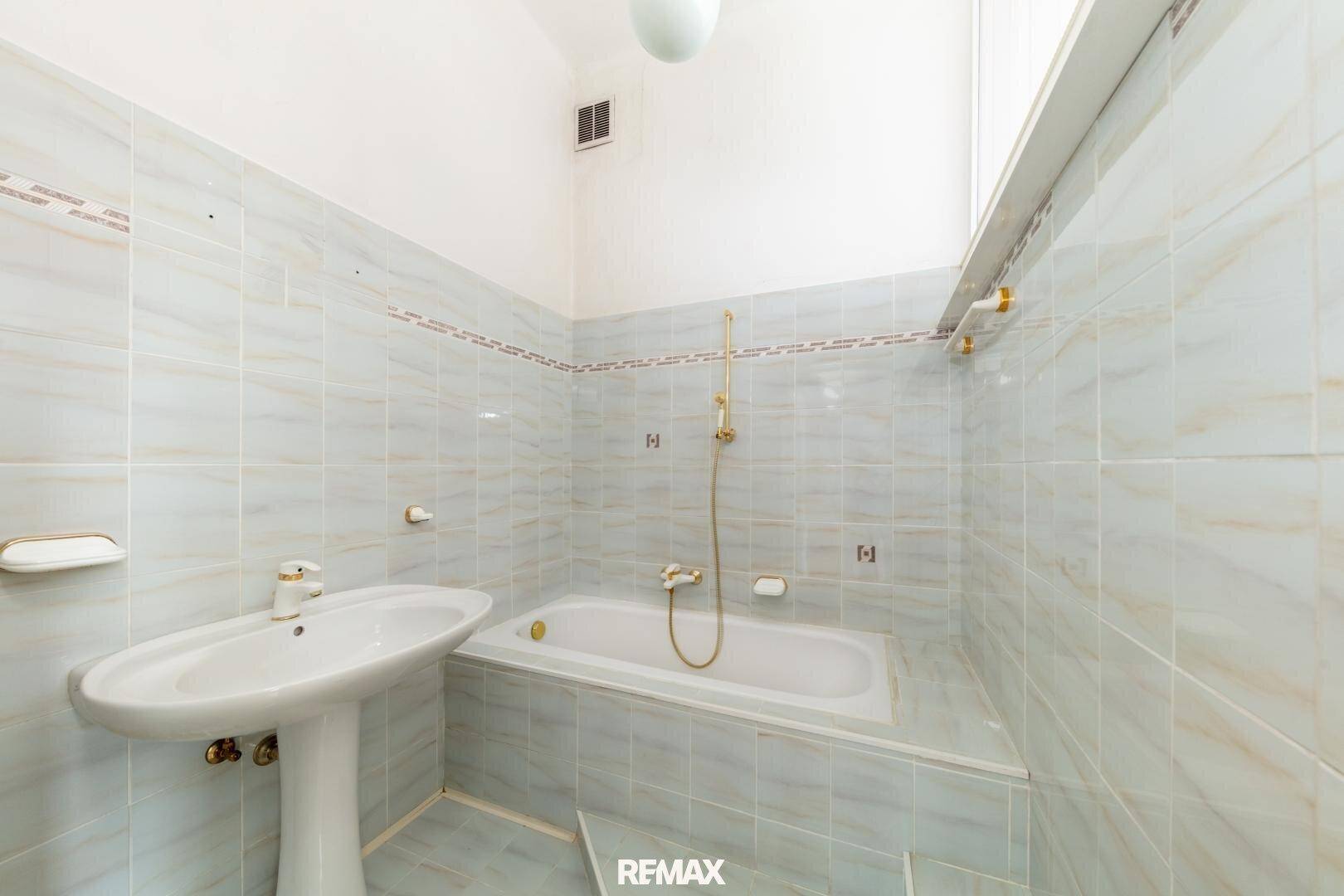 Badezimmer mit hellblauen Fliesen, Badewanne und Waschtisch, im Stil der 80er Jahre.