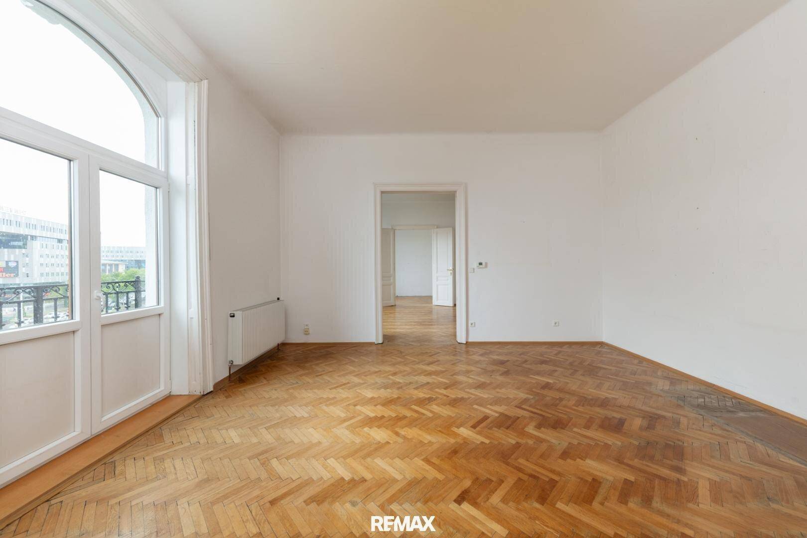 Geräumiges Zimmer mit Fischgrätparkett und Zugang zu einem französischen Balkon.